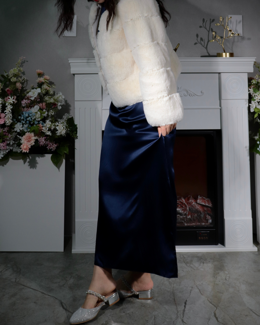 Woman standing, showcasing the elegant fit and luxurious drape of a Midnight Navy 100% mulberry silk maxi dress, gently holding the edge of the flowing fabric. This image highlights the smooth texture and subtle sheen of the dress, paired with embellished low-heeled shoes, suitable for evening wear or sophisticated events.